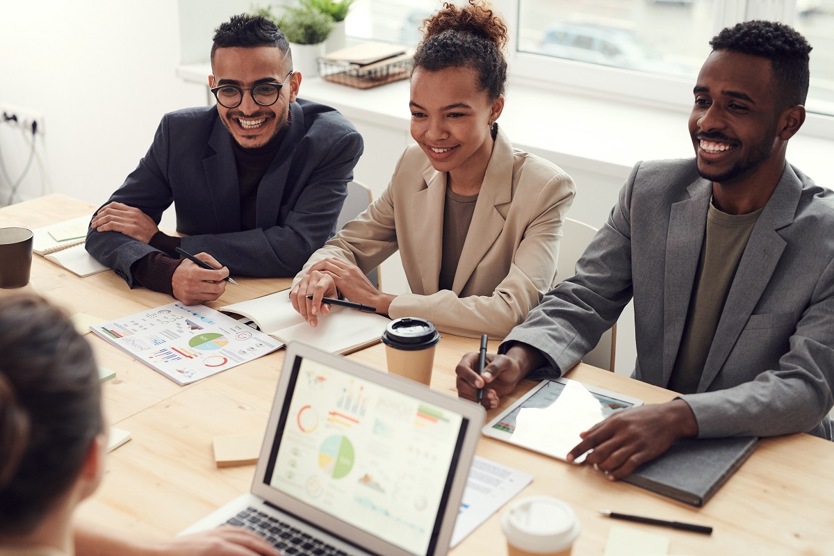 Executivos e executivas sentados ao redor de uma mesa com notebooks, papéis e canetas