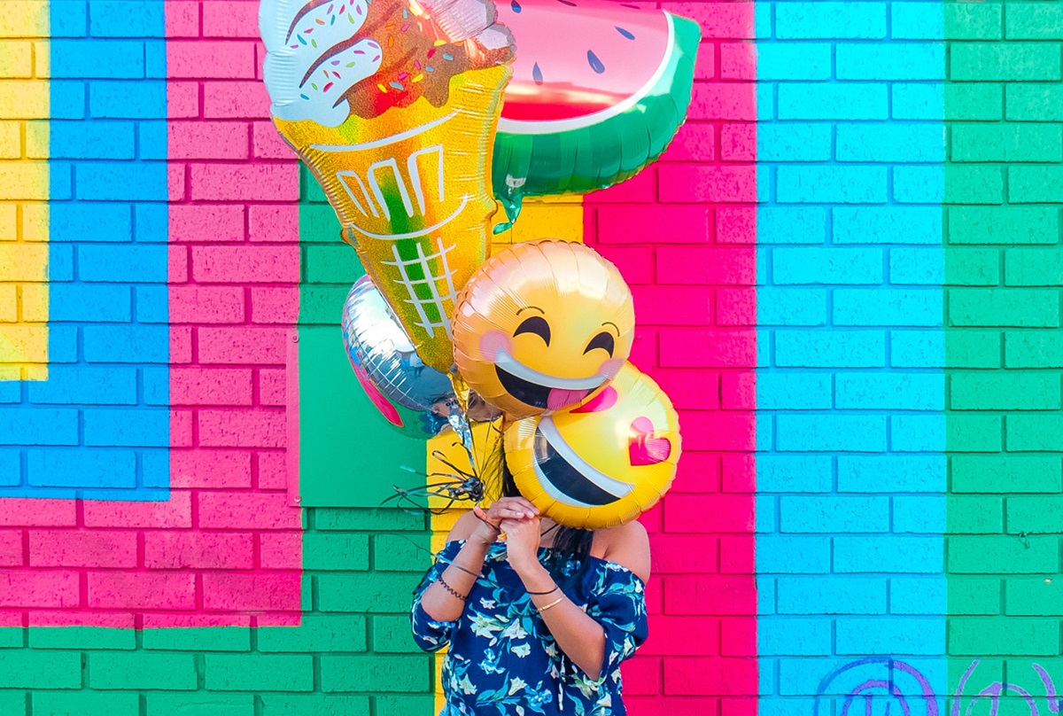 Pessoa com diversos balões com temáticas de carinha feliz e frutas nas mãos