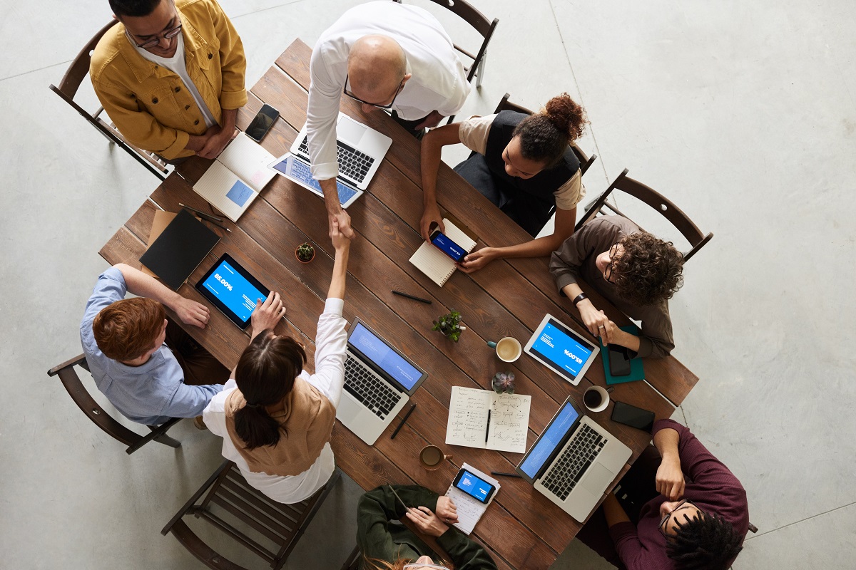 Pessoas com computadores ao redor de uma mesa enquanto duas delas se cumprimentam com um aperto de mãos