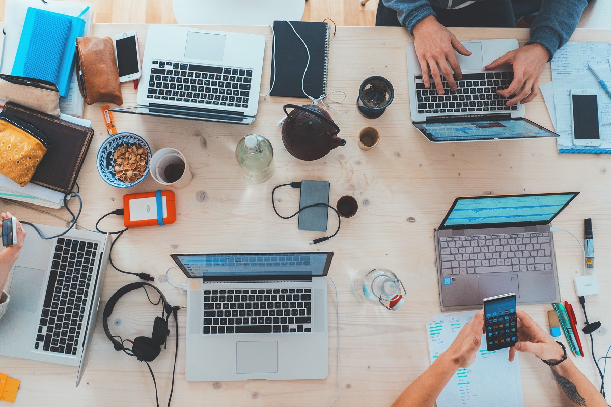 Pessoas sentadas ao redor de uma mesa com notebooks, smartphones e phones