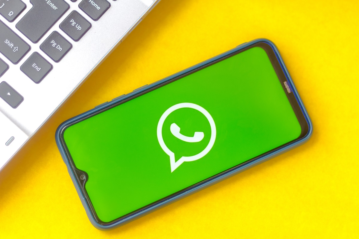 Celular com o WhatsApp aberto sobre uma mesa com fundo amarelo e uma parte do teclado de um notebook