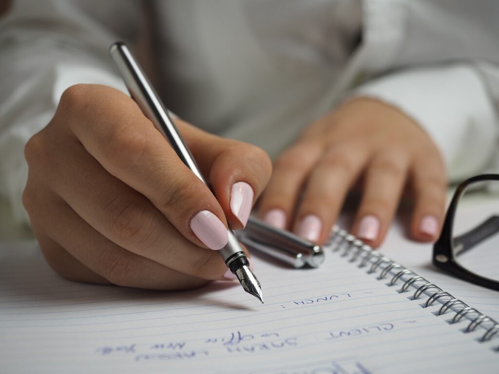 Pessoa escrevendo com caneta em caderno