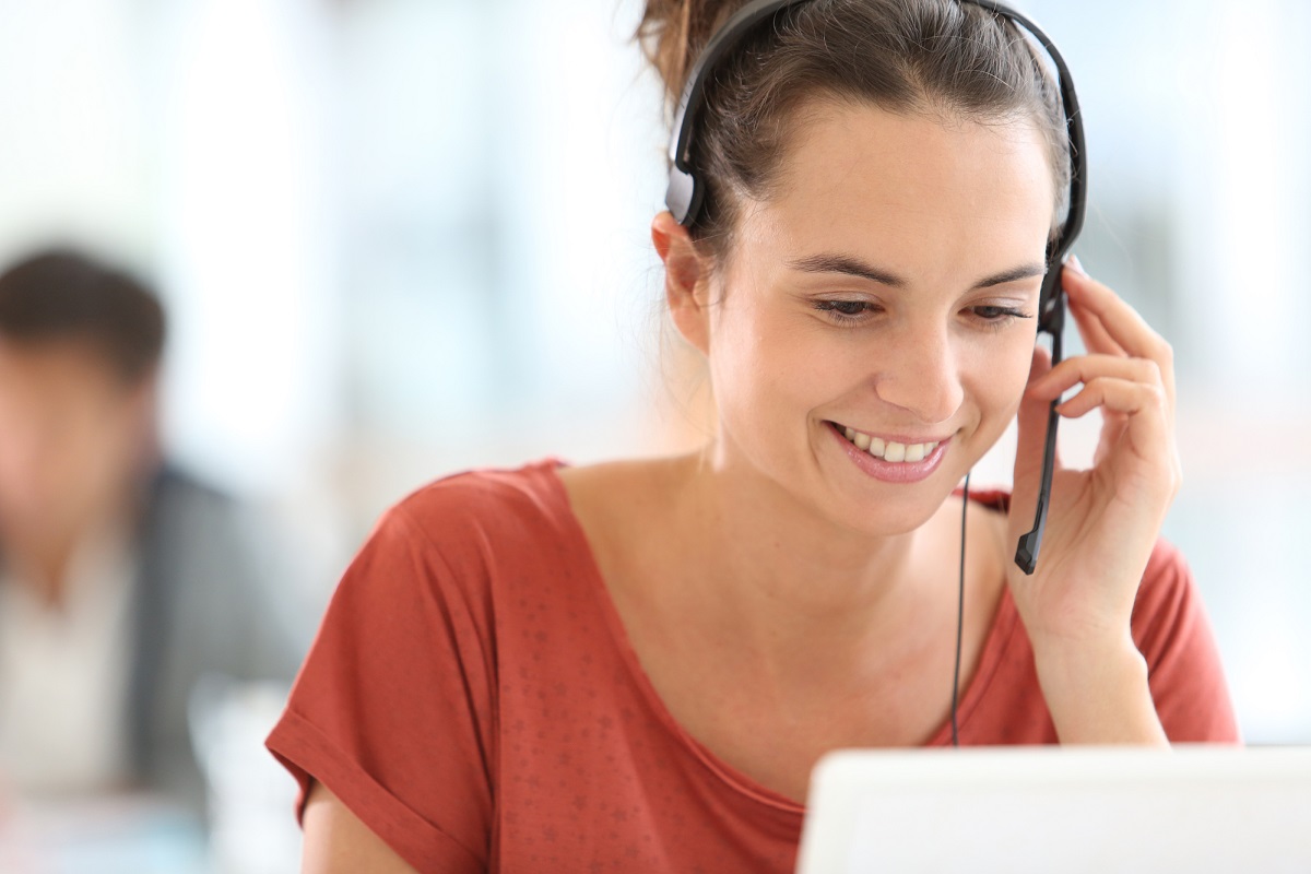 Mulher com headset olhando para uma tela de computador e sorrindo