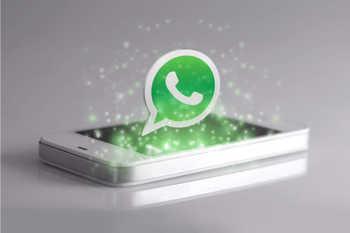 Celular sobre uma superfície plana na cor cinza com o logo do WhatsApp saindo do aparelho.