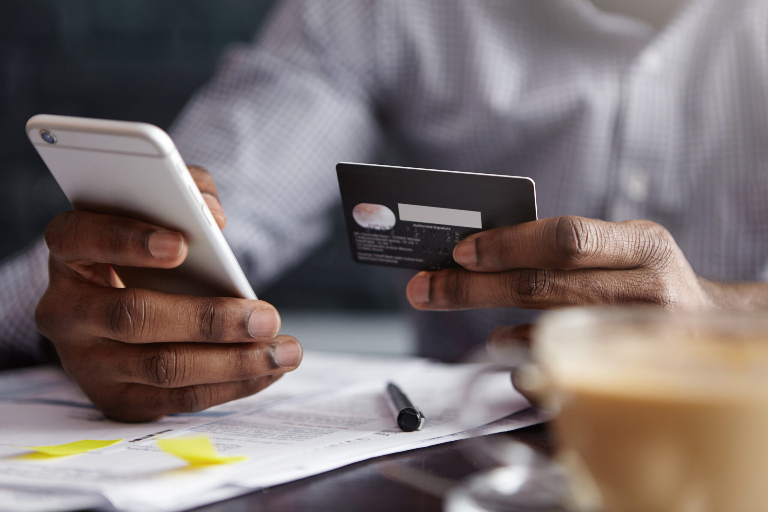 homem negro segurando celular e cartão de crédito na mesa de uma café