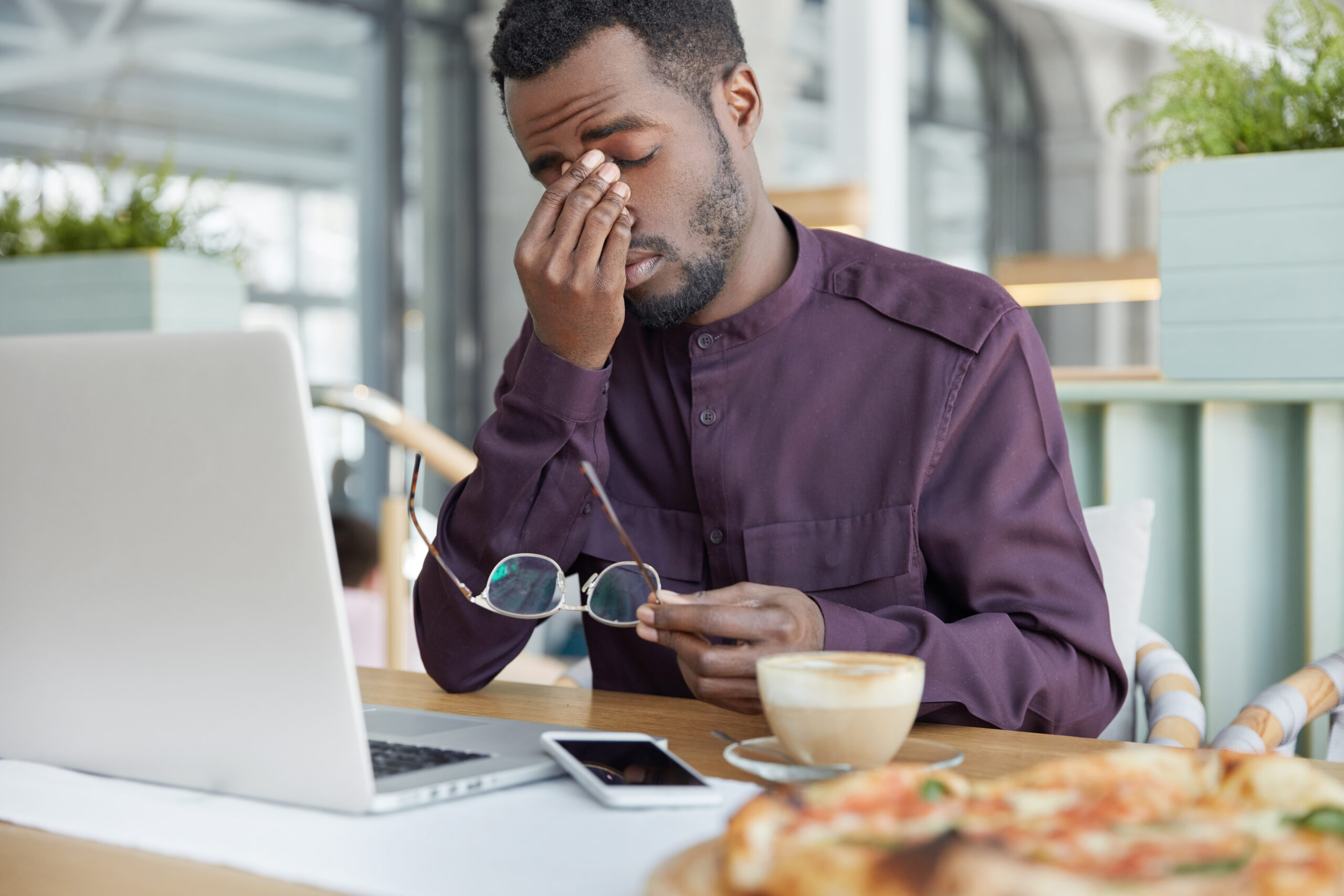 Economista profissional sobrecarregado, segura os óculos, estando cansado de trabalhar no laptop por muitas horas, tem dor de cabeça após um dia cansativo de trabalho