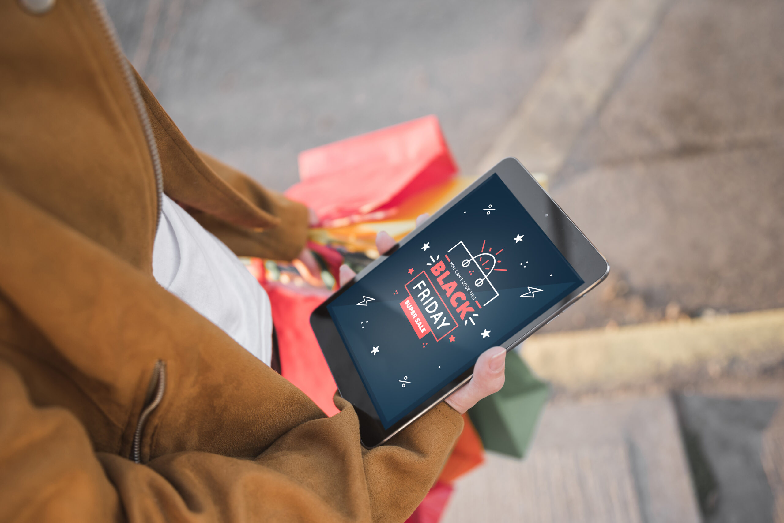 mulher segurando sacolas de compras e tablet com escrito "Black Friday" na tela